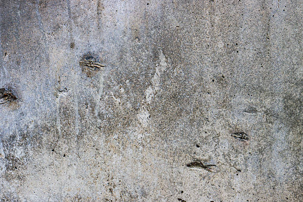 Close-up of a textured concrete wall with rough, uneven surfaces and a mix of gray and brown tones, showcasing natural imperfections and patterns.