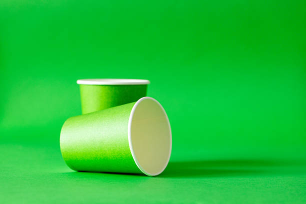 Row of disposable cups and straw on white background. Minimal flat lay composition of green plastic glasses with copy space.