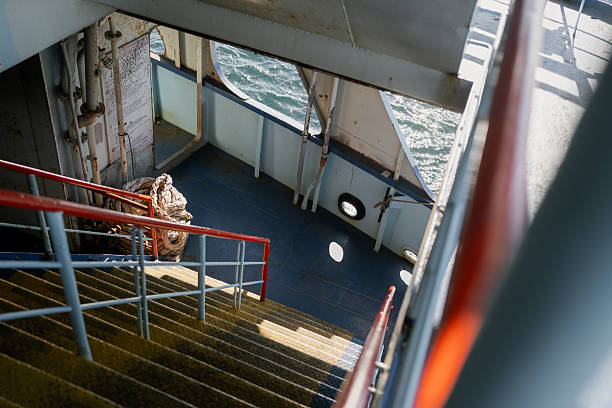 Looking down a staircase on a ferry boat, with a glimpse of the ocean through the open deck and a coiled rope nearby