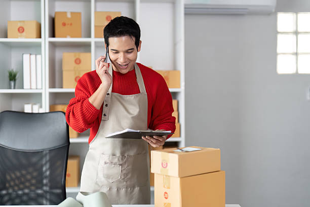 istock E-commerce Operations and Customer Engagement. A young entrepreneur prepares a shipment while taking notes during a logistics call. 2214610384