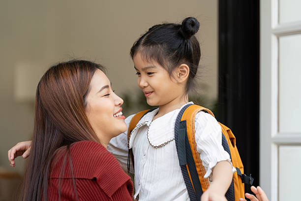 A touching interaction between a mother and her daughter, both smiling as the little girl prepares her backpack for school. Their joyous expressions reflect a loving bond and guidance.