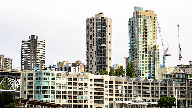 A scenic view of Vancouver’s False Creek marina with boats and yachts docked in the foreground and a backdrop of modern glass skyscrapers and high-rise residential buildings. The overcast sky adds a soft, diffused light to the scene, emphasizing the vibrant urban architecture and tranquil waters. This image captures the essence of life in a thriving West Coast city, ideal for use in travel, real estate, urban planning, architecture, and lifestyle content.