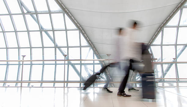 istock A people with luggage walking in motion blur on white corridor with large windows. Blurred people walking in a modern building. Abstract image of people in the lobby. 2214619740