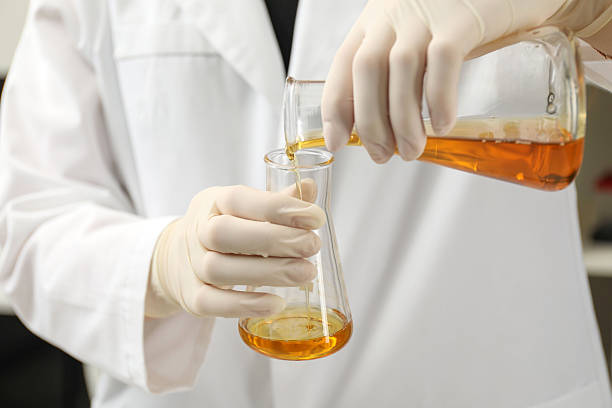 istock Laboratory worker pouring orange crude oil into flask, closeup 2214620594