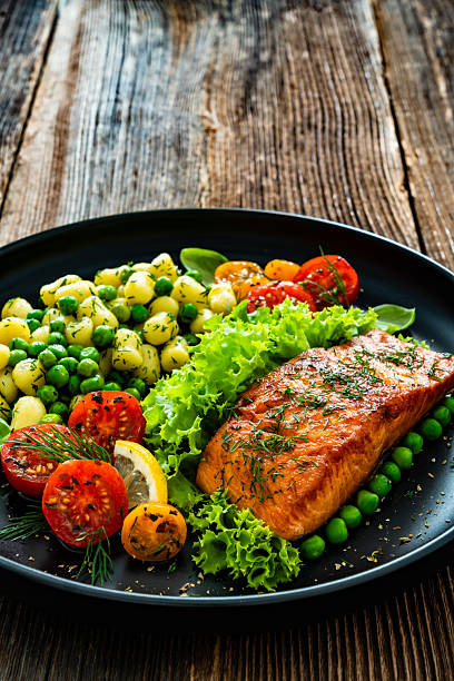 Seared salmon steak with gnocchi and fresh vegetables served on black plate on wooden table