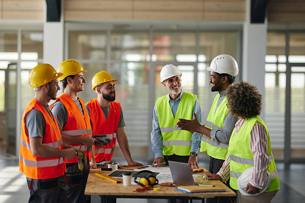istock Team of happy architects and manual workers talking at construction site. 2214627700