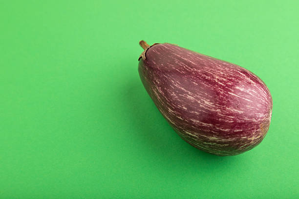 Purple eggplant with white stripes on green pastel background. Side view, copy space. Tropical, healthy food, vegetable, minimalism.