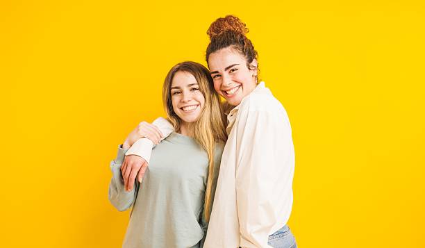 istock Two smiling young women embracing on yellow background 2214635858