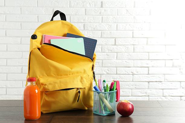 istock Backpack with different school stationery, apple and juice on wooden table against brick wall 2214636145