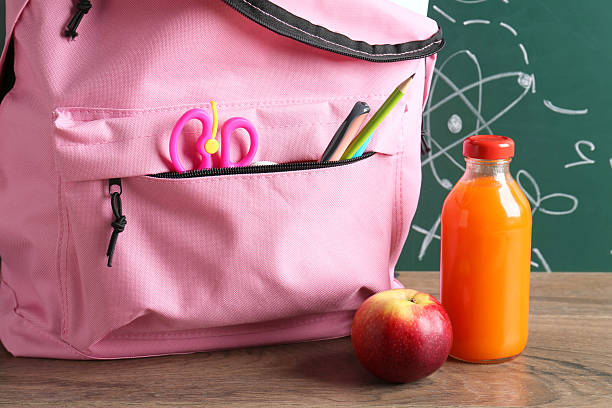 istock Backpack with different school stationery, apple and juice on wooden table against green chalkboard 2214636211