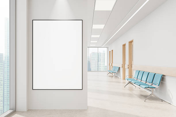 istock Blank vertical poster mockup on clean white wall in modern hospital corridor with blue chairs and wood doors, large windows with city view. 3D Rendering 2214636821