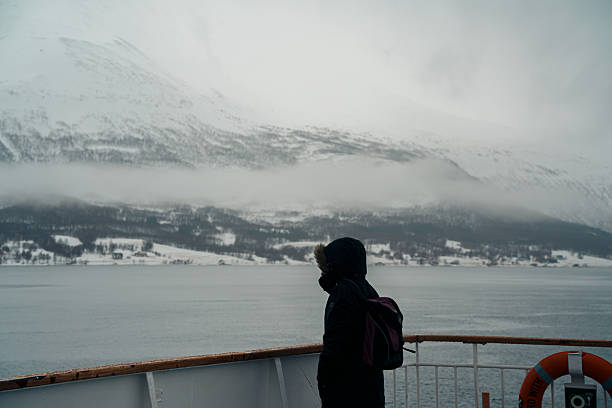 Tromso, Norway - APR 9,2024: Travelers onboard the Hurtigruten cruise admire snowy fjords and misty mountain landscapes during a winter voyage from Lofoten to Tromsø.