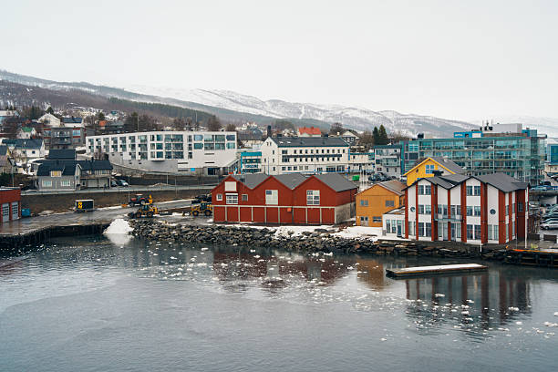 Tromso, Norway - APR 9,2024: Scenic view of Finnsnes, Norway, captured from the Hurtigruten cruise with colorful buildings, snowy hills, icy water, and coastal industry.