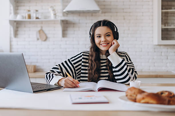 istock Smiling female student studying online using a headset, laptop sitting at kitchen posing at camera 2214641703