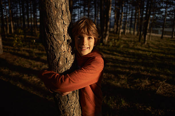 Beautiful boy hugging tree in nature.
