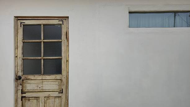 2️⃣ A weathered wooden door with glass panels and a high-positioned window stand against a white wall, evoking a simple yet elegant architectural style.