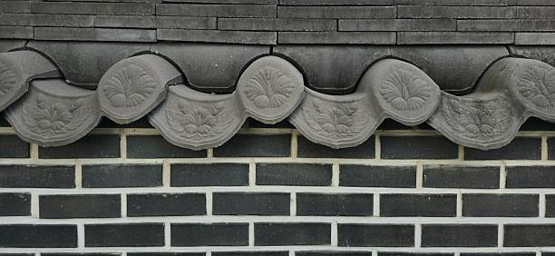 Elegant Korean roof tiles adorned with floral engravings rest upon a clean brick wall, showcasing timeless craftsmanship and harmony.