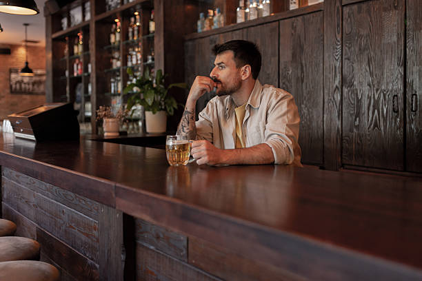 istock Young Man Alone in Pub, Drinking Beer, Looking Depressed 2214644590