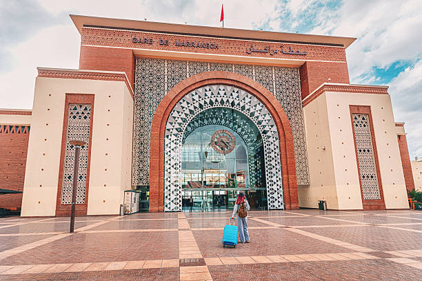 05 March 2025, Marrakech, Morocco: Young woman pulling suitcase walking towards the modern railway station