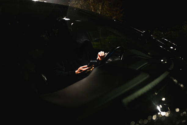 Hooded criminal using smartphone while driving car at night