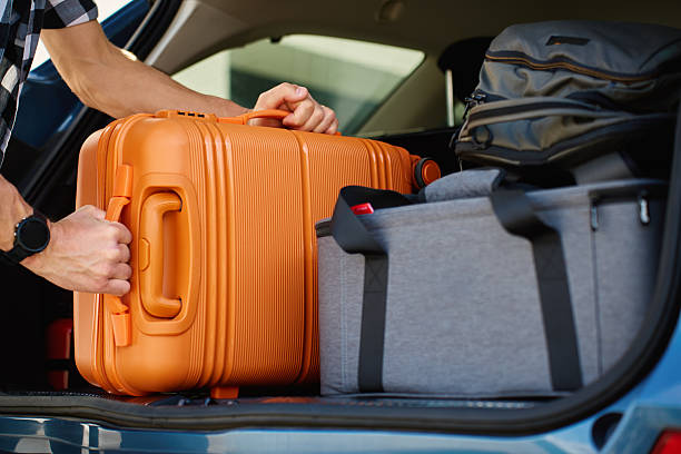 Man loading orange suitcase into car trunk before journey. Packing luggage for travel