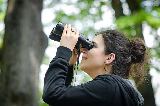 istock Standing beneath tall trees, a woman scans the branches with binoculars, searching for birds and nests above. The moment captures her quiet connection with wildlife and nature. 2214663745