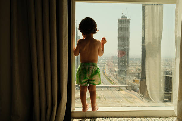 Toddler standing on a window sill, gazing at Dubai's stunning cityscape from a high-rise building, filled with wonder and curiosity