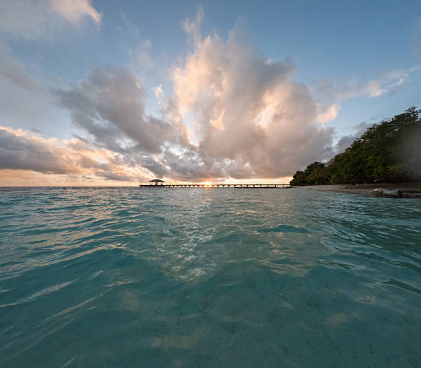 Wooden pier extending into the Indian Ocean, surrounded by vibrant tropical scenery, showcasing a breathtaking sunset with dramatic clouds