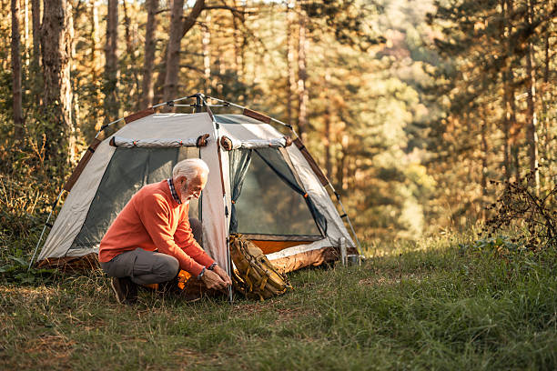 istock Senior Man Camping in Forest Setting Up Tent During a Tranquil Afternoon 2214668900