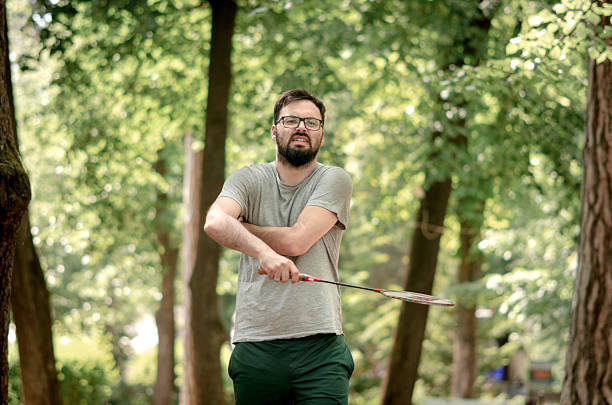 While playing badminton, a man feels a strain in his shoulder, taking a break to stretch. The image reflects both the intensity of outdoor sports and the need to listen to your body.