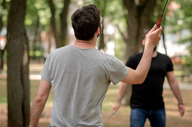 In a wide open field, two men play badminton with energy and focus, showcasing their athleticism. The clear skies and fresh air make it an ideal moment for outdoor fitness and recreation.