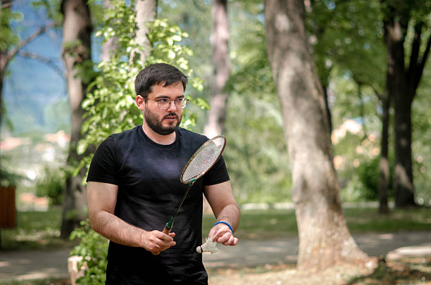 On a vibrant, sunny day, a man swings his badminton racket, enjoying a fun outdoor game. The scene highlights health, sportsmanship, and the joy of staying active in nature.