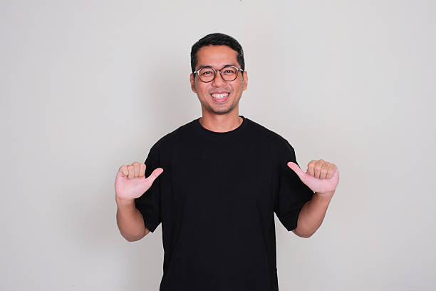 istock A man smiling proud while pointing at his plain black t'shirt that he wear 2214683271