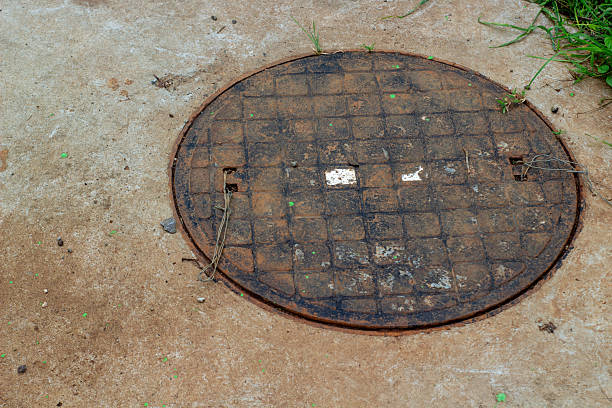 Rusty, weathered sewage iron manhole cover set in concrete