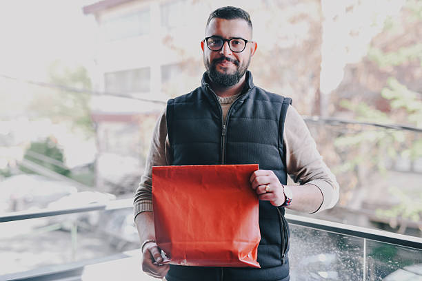 istock Handsome Male Holding Red Paper Bag Looking at Camera With Smile 2214689677