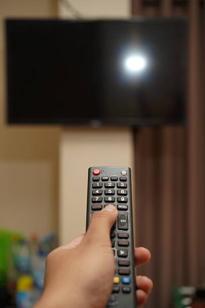 istock Selective focus on man hand hold remote control and turn on tv panel with mockup display 2214690717