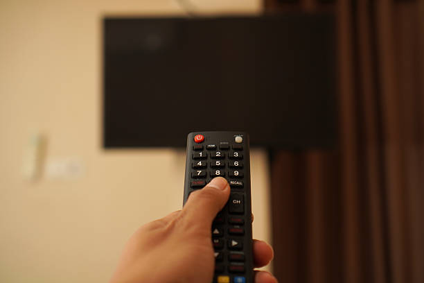 istock Selective focus on man hand hold remote control and turn on tv panel with mockup display 2214690732