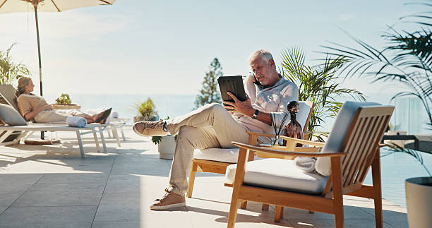 istock Phone call, tablet and reading with man at hotel for remote work, resort critic and customer feedback. Relax, freelancer and hospitality review with mature person at villa for luxury travel research 2214692559