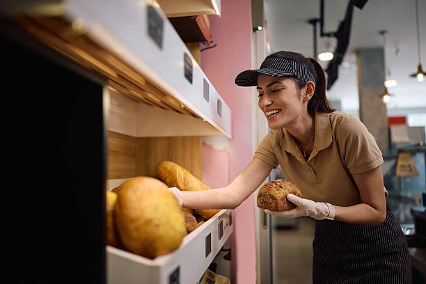 istock Happy female baker arranging fresh bread on shelves in a bakery. 2214696627