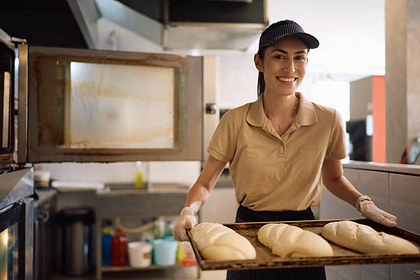 istock Happy female baker baking pastry in the oven and looking at camera. 2214697697