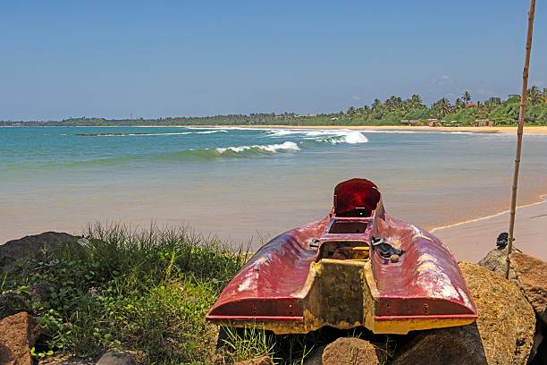 Red abandoned boat on rocks at tropical beach facing gentle surf in summer