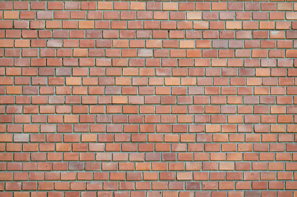 A straight-on view of a traditional brick wall composed of red, orange, and light brown bricks arranged in a uniform horizontal pattern. The slight variations in color and texture add depth and visual interest, making it a classic example of masonry in architectural design. The image serves as a versatile urban background.