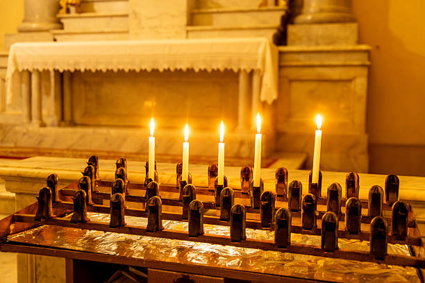Six lit candles placed in a metal holder in front of a marble altar inside a church in Oristano, casting a warm glow in the sacred space.