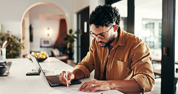 istock Finance, man and laptop with writing in home for financial assessment, account summary and budgeting. Paperwork, planning and asset management with investment portfolio, statement report and expenses 2214707229
