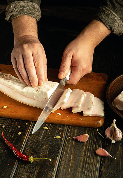 istock Hands skillfully slice fresh pork belly on a cutting board, surrounded by garlic cloves and dried chilies. The rustic kitchen adds to the authentic cooking atmosphere 2214708011