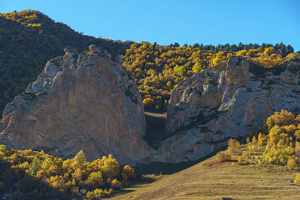 Picturesque landscape featuring towering rock formations and vibrant autumn foliage, with clear blue sky enhancing the natural beauty of scene. Kabardino-Balkaria. El-Tyubu