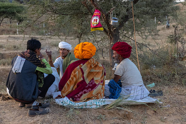 Pushkar, Rajasthan, India - November 2024: Group of a rajasthani male in traditional white clothes with colourful turban at desert ground in winter morning with camel during pushkar fair.