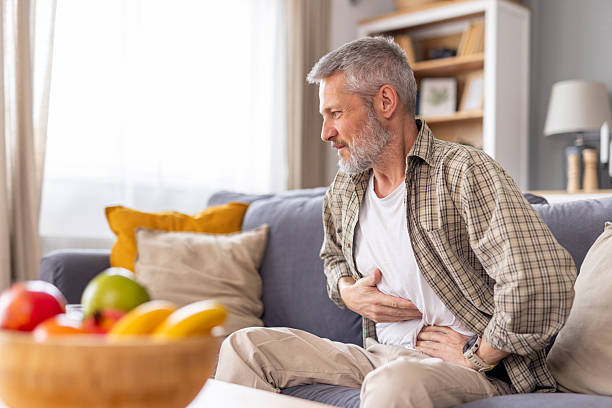 Man experiencing stomach pain while seated on the couch.