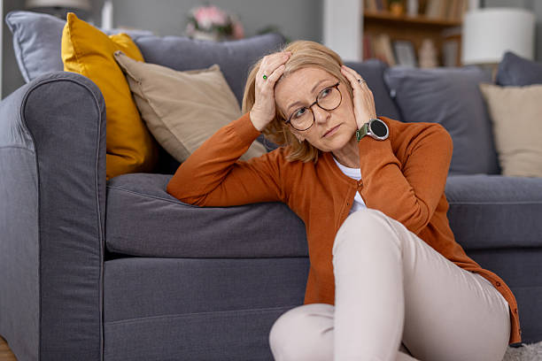 istock Concerned woman sitting on couch holding her head in stress 2214717098