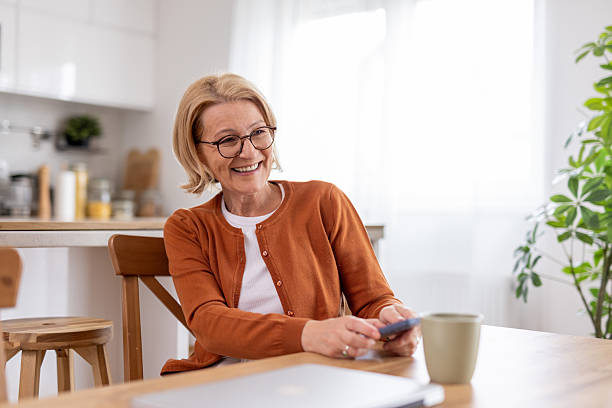 istock Joyful senior woman with a phone in a cozy kitchen space. 2214717104